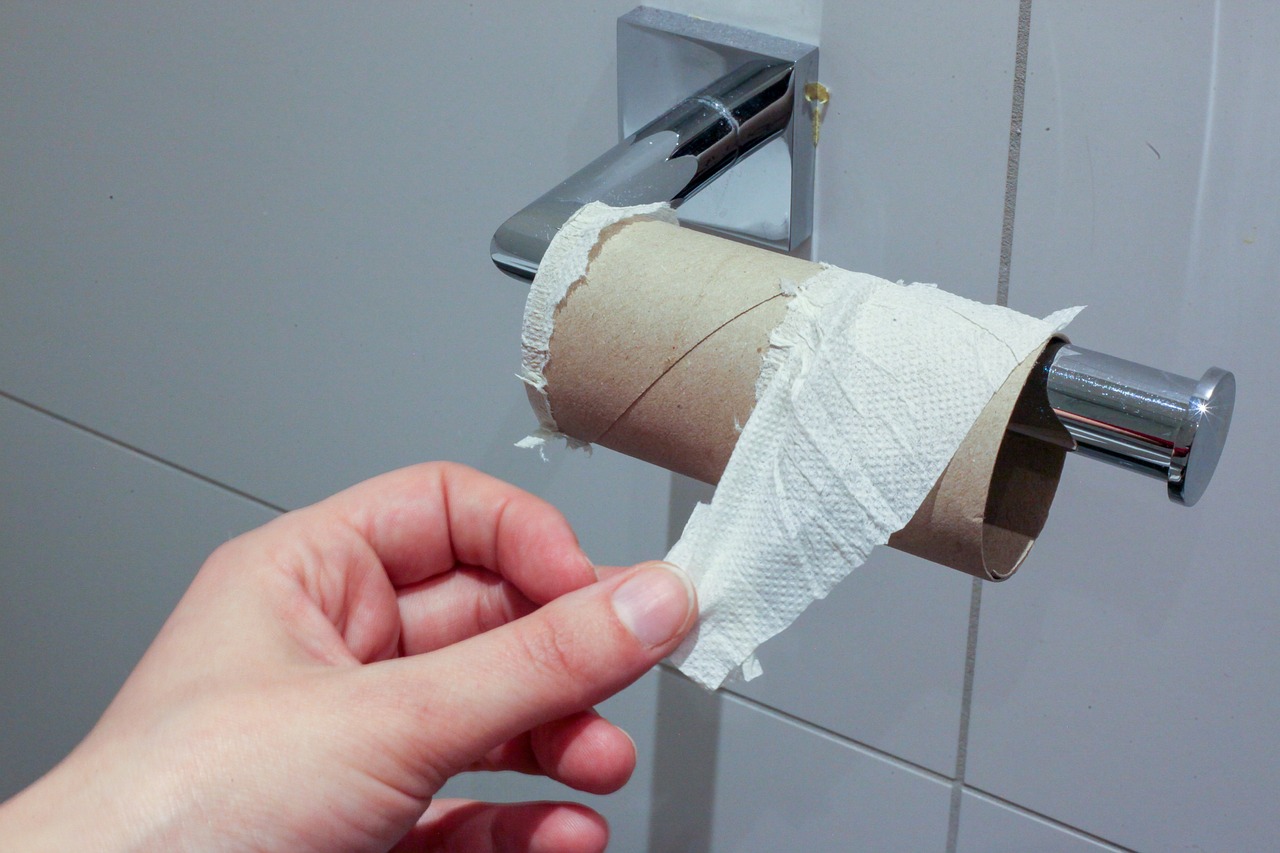 Hand pulling the last bit of toilet paper from an empty roll, a common cause of toilet clogs.